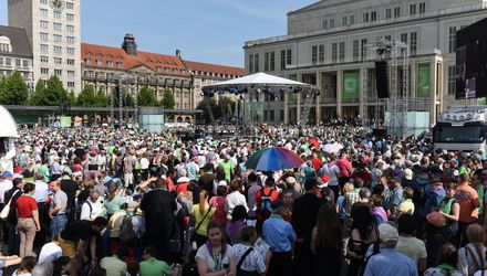 Der sonnenbeschienene Platz ist voller Gottesdienstbesuchern, man sieht Richtung Altarraum.