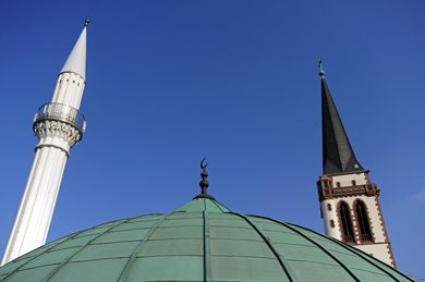 Minarett und Kirchturm ragen in den blauen Himmel.